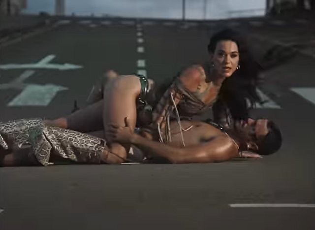 Katy Perry on top of a man in the middle of the road in music video 